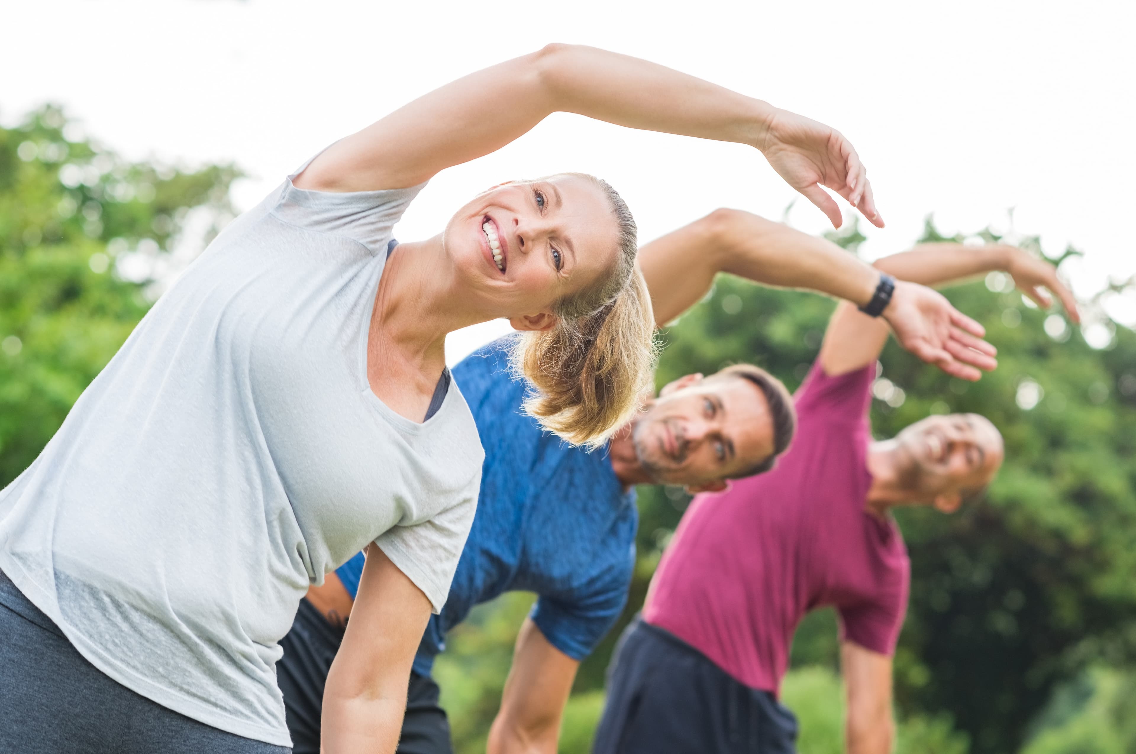 A group of active adults stretching and exercising outdoors together on a bright day