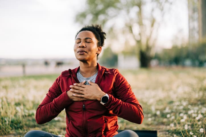 A woman relaxing outdoors at golden hour with her hands over her heart, feeling restored